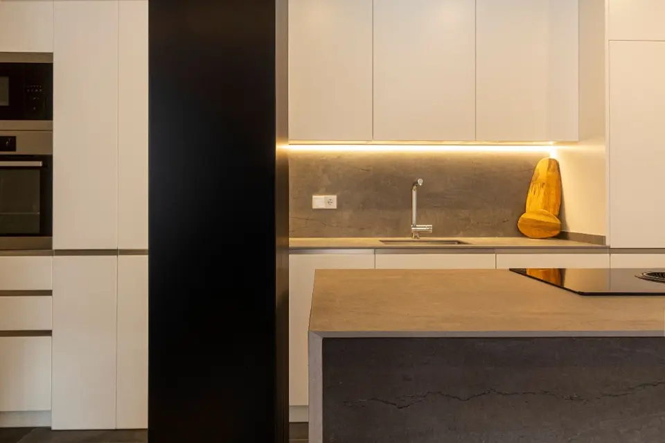 Cocina minimalista blanca con encimera de piedra y columna negra